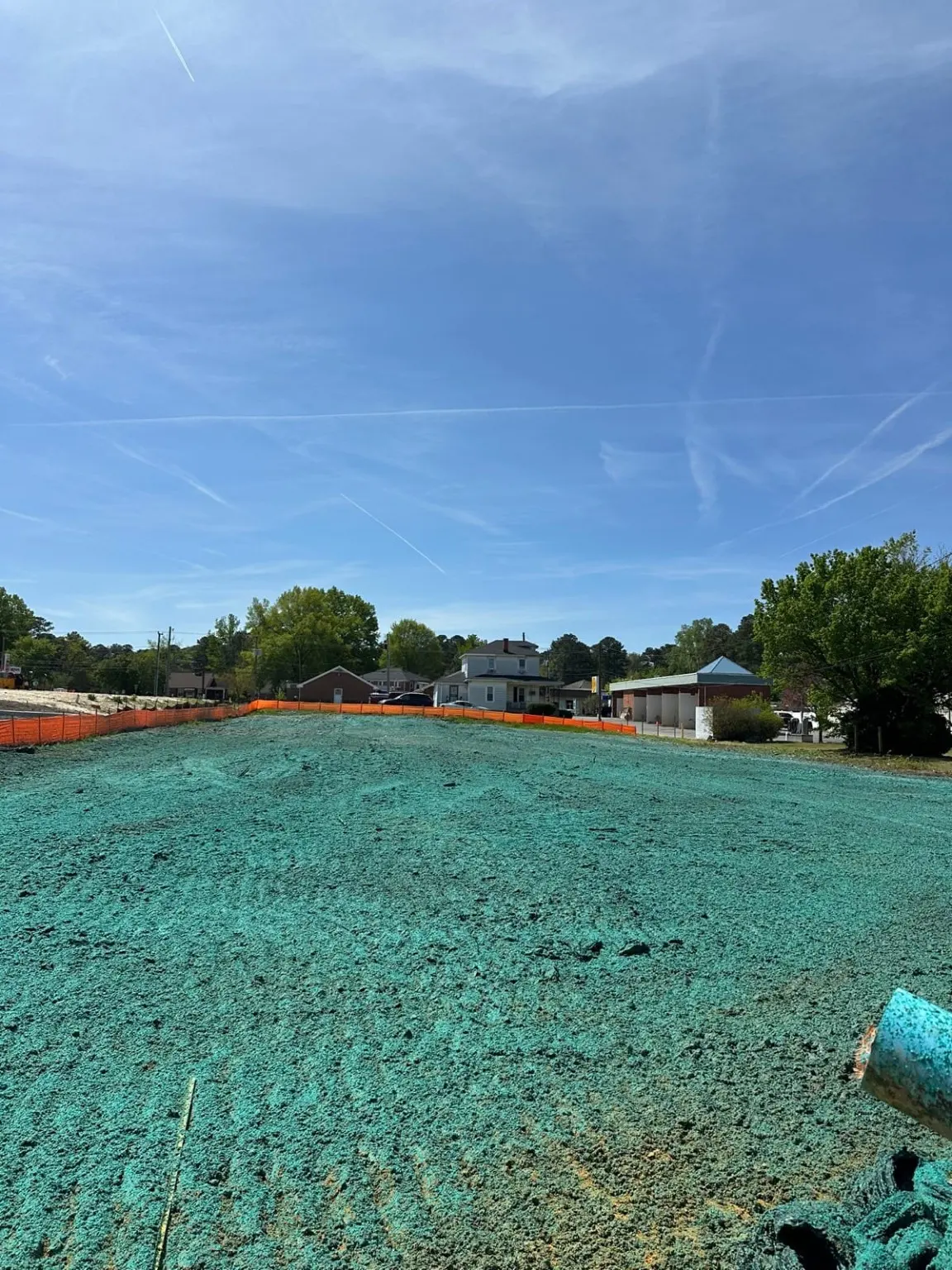 A graded area covered with blue-green hydroseeding mulch behind orange fencing.