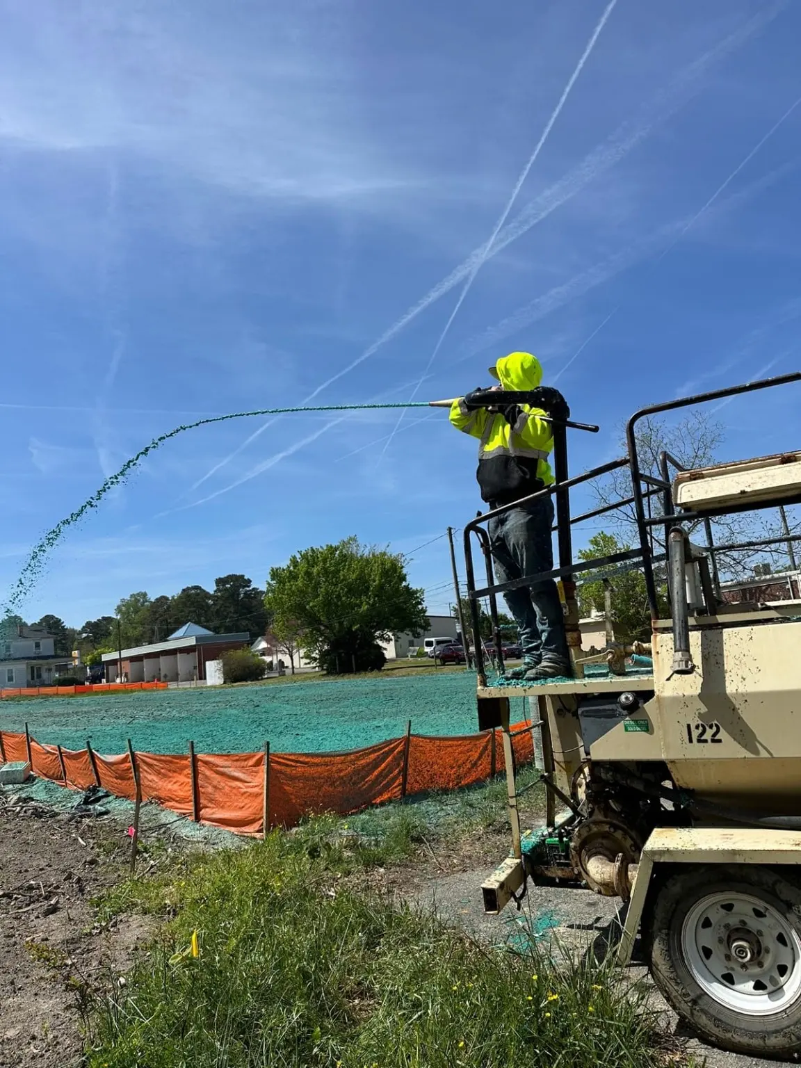 A worker applies hydroseeding mulch from a spray platform.