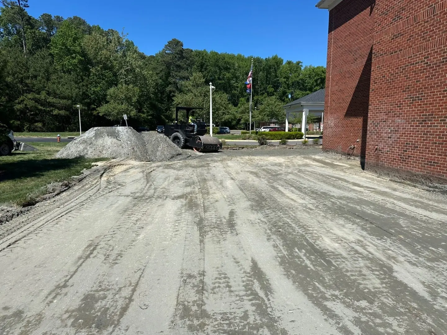 An aggregate work area with a roller and material stockpile beside a brick building.